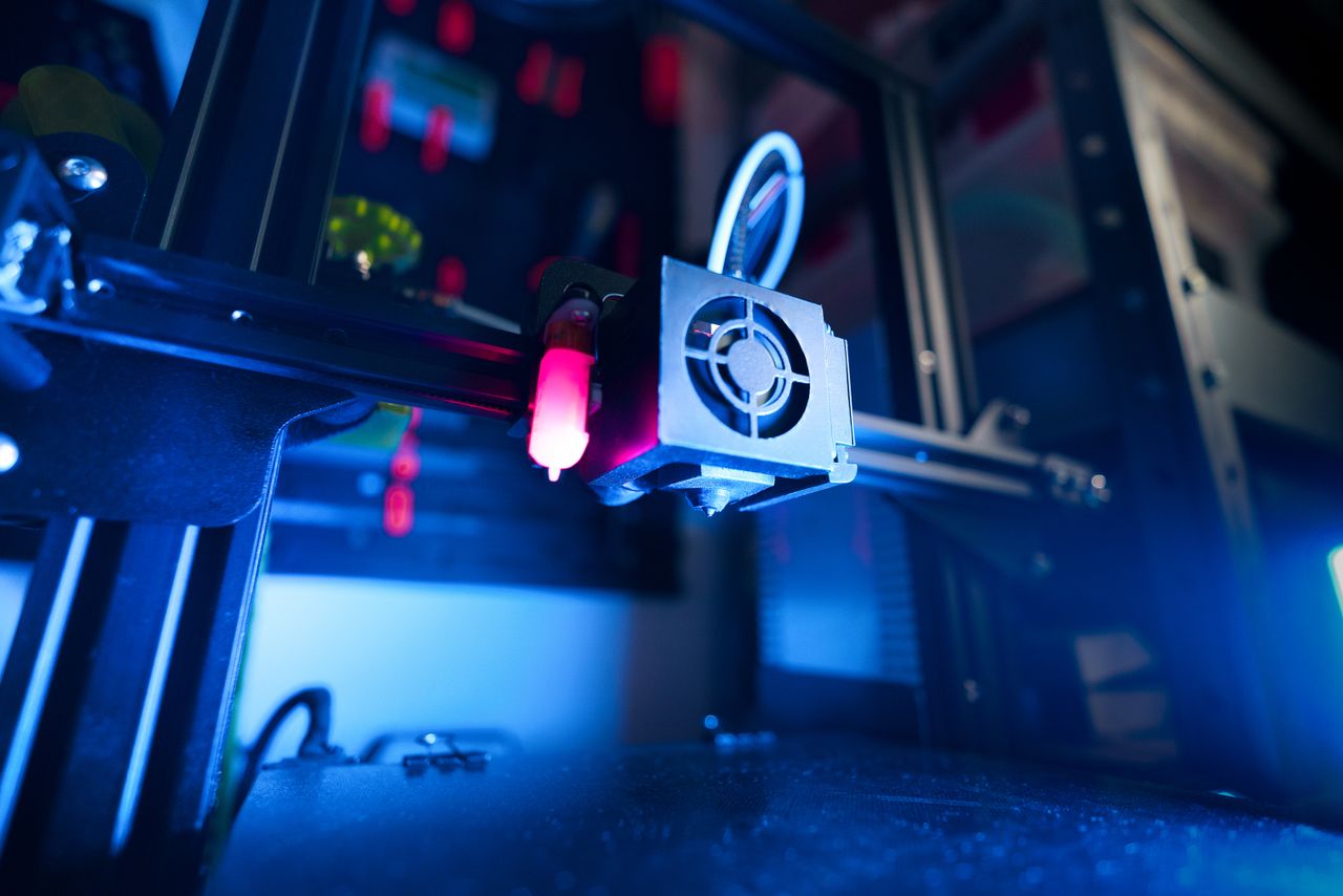 hero-img-01 A close-up of an illuminated 3D printer in action, highlighting modern technology.
