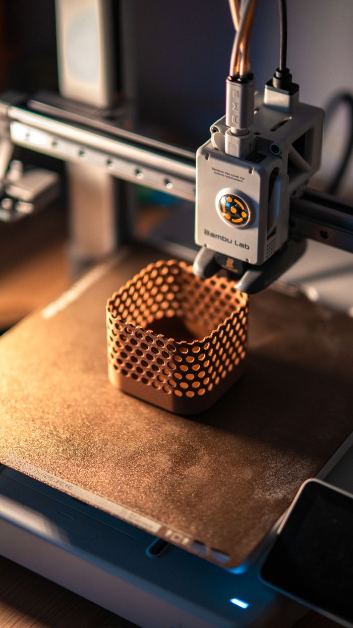 services-03 Close-up of a 3D printer creating a hexagonal object in a dimly lit workspace.