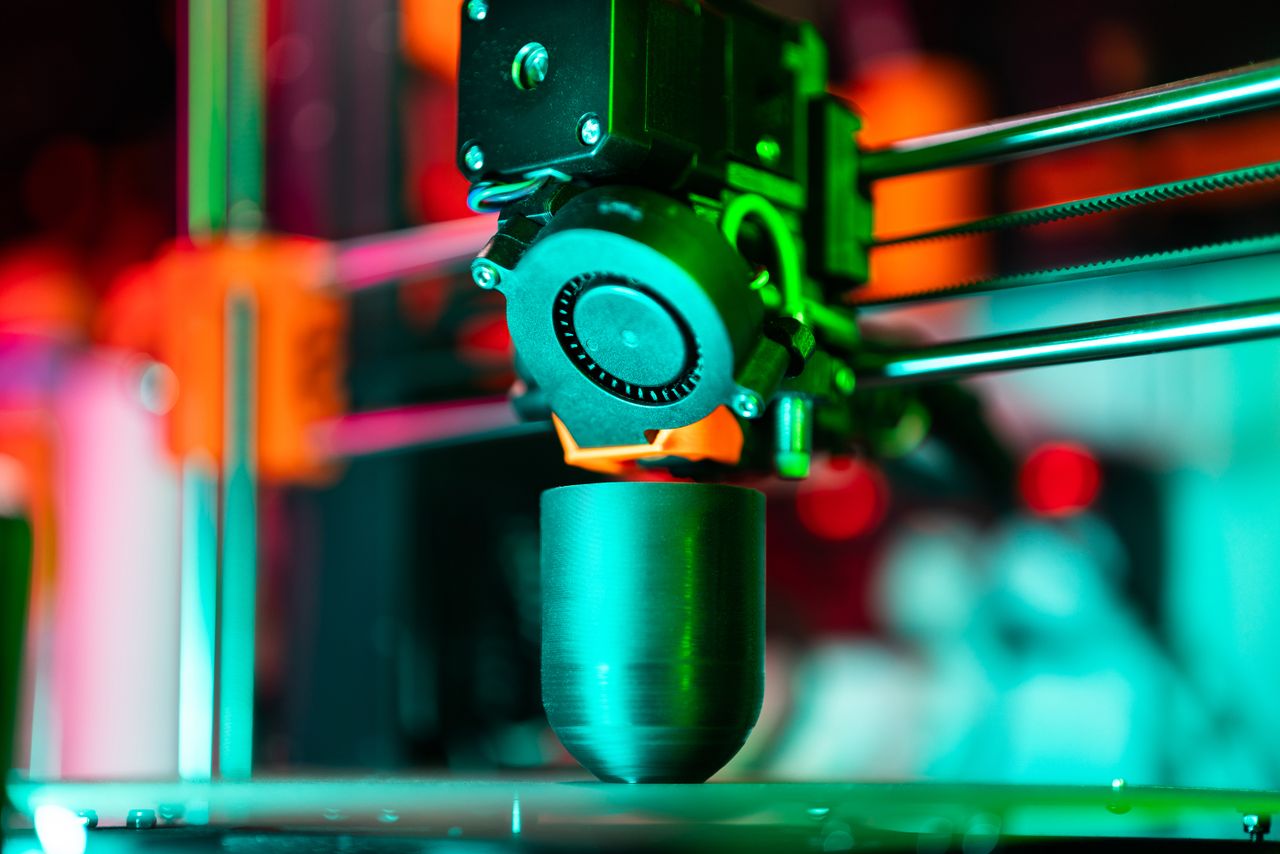 about-01 Close-up of a 3D printer creating a product in neon lighting.