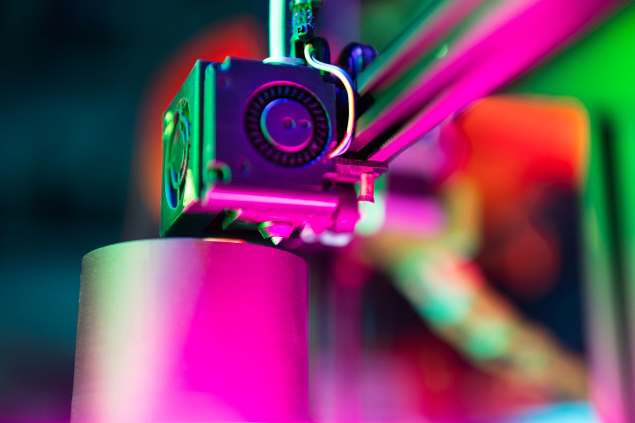 hero-img-02 Close-up of a 3D printer in action under neon lighting, capturing vibrant colors and modern tech ambiance.