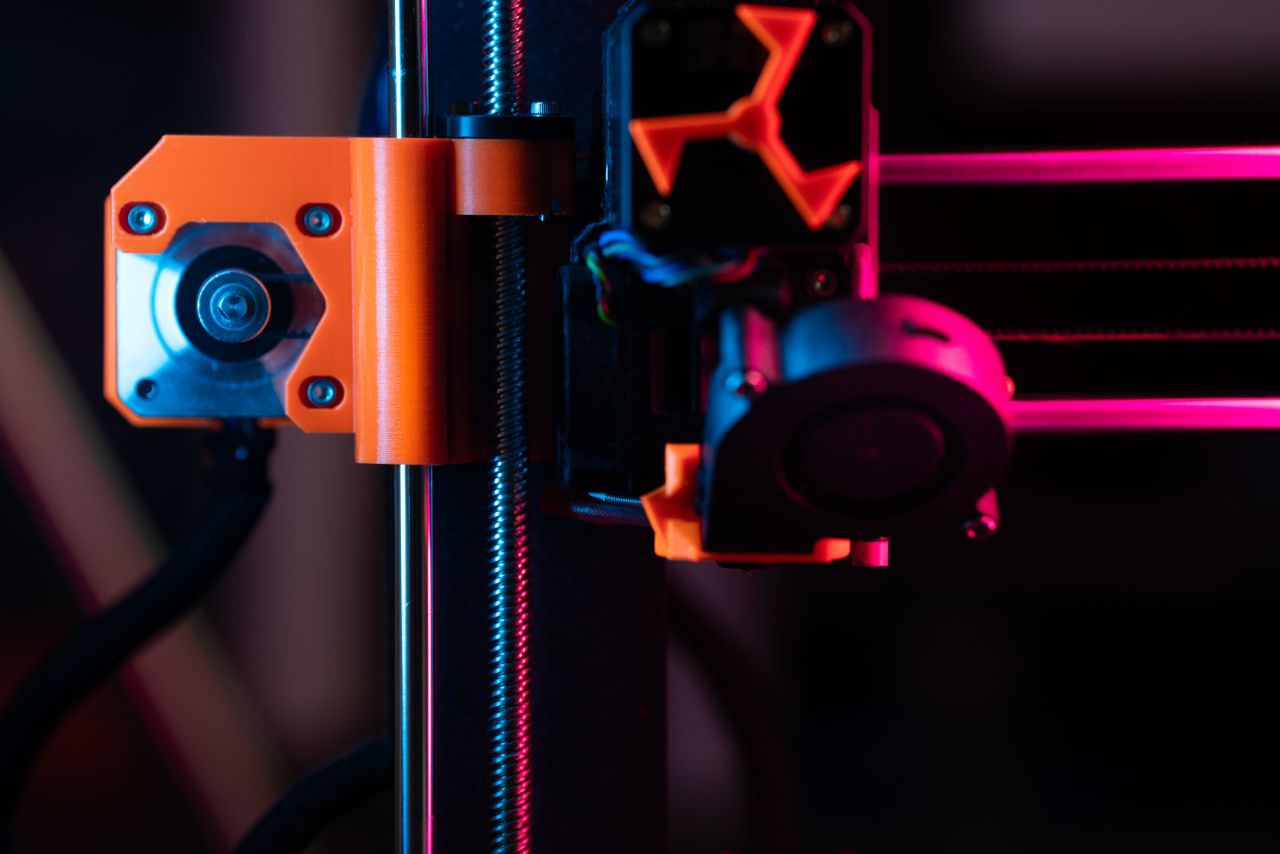 gallery-5 A detailed close-up of a 3D printer showcasing its extruder and components under vibrant lighting.